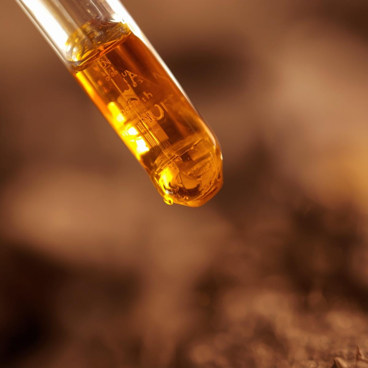 Close-up of a glass vial with a yellowish liquid against a blurred background