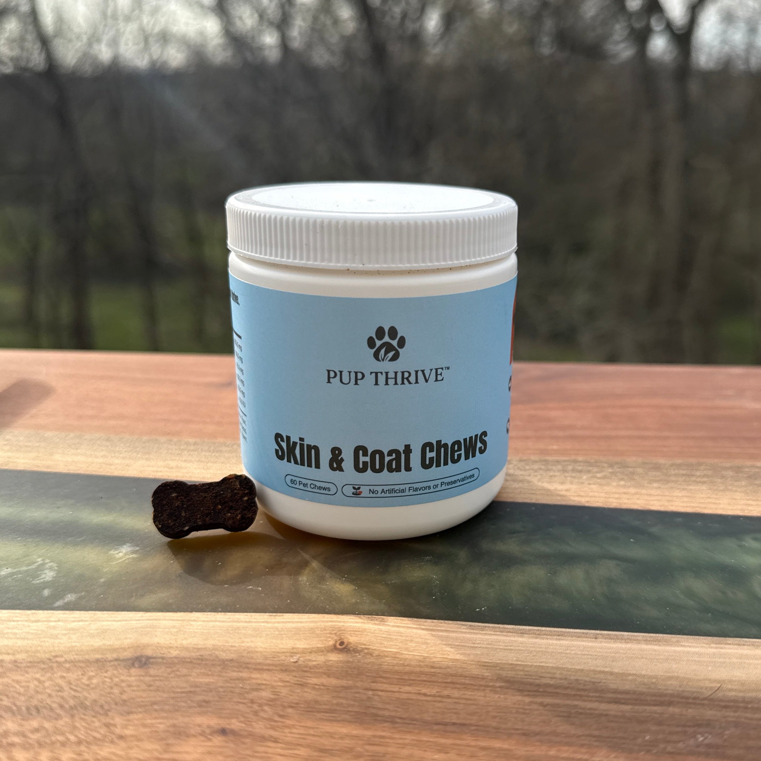 Container of 'Pup Thrive Skin & Coat Chews' on a wooden surface with a blurred outdoor background.
